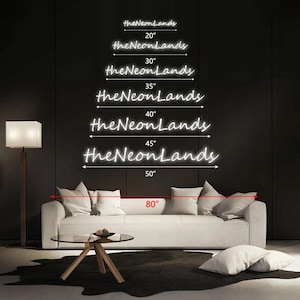 Pu&ograve; includere: Opzioni di insegne al neon bianche da "theNeonLands" con dimensioni da 50.8 cm a 127 cm. L'immagine mostra anche una misura di 203.2 cm. Le insegne sono esposte su uno sfondo scuro, sopra un divano bianco con cuscini, un tavolino di vetro e una lampada da terra.