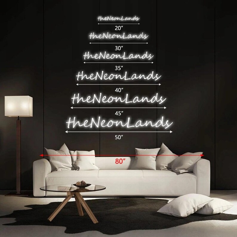 Pu&ograve; includere: Opzioni di insegne al neon bianche da "theNeonLands" con dimensioni da 50.8 cm a 127 cm. L'immagine mostra anche una misura di 203.2 cm. Le insegne sono esposte su uno sfondo scuro, sopra un divano bianco con cuscini, un tavolino di vetro e una lampada da terra.
