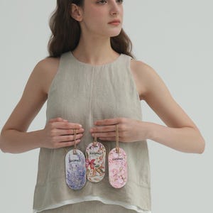 Könnte beinhalten: Drei ovale Lufterfrischer mit floralen Designs und dem Aufdruck "EUOPHO". Die Lufterfrischer sind lavendelfarben, floral und rosa. Sie sind an Schnüren aufgehängt.