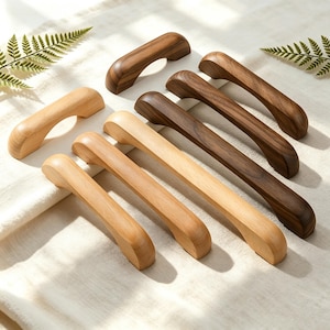 May include: A collection of seven wooden cabinet handles arranged in two rows. Four handles are crafted from a light-toned wood, while three handles are made from a darker, rich-toned wood. Each handle features a smooth, curved, arching design.