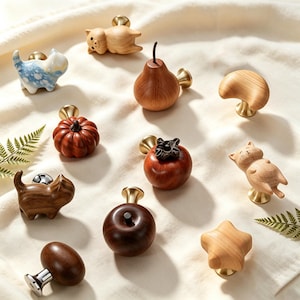 Peut inclure: Une collection de boutons de placard décoratifs présentant diverses formes, dont un cochon en bois clair, un chat en céramique bleu et blanc, une poire en bois, un croissant de lune, une citrouille, un kaki, un chat, une étoile et une pomme en bois foncé.