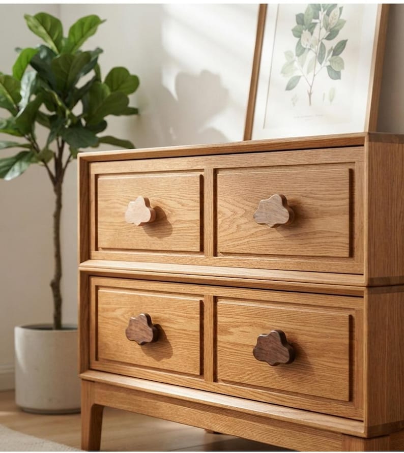 May include: A light brown wooden dresser featuring four rectangular drawers with raised borders. Each drawer is equipped with a dark brown wooden knob shaped like a cloud. The dresser has a natural wood grain finish and stands on four short legs.