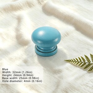 Puede incluir: Un pomo de madera redondo de color azul claro con un acabado liso. El pomo tiene un ancho de 32 mm, una altura de 24 mm, un ancho de base de 25 mm y un di&aacute;metro de orificio de 4 mm, tal como se indica en el texto impreso.