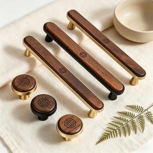 Könnte beinhalten: Eine Sammlung von Holzmöbelbeschlägen, darunter Griffe und Knöpfe. Die Griffe haben eine dunkle Holzmitte mit goldenen oder schwarzen Akzenten. Die Knöpfe sind rund mit passender Holzoberfläche und goldenen oder schwarzen Basen. Jedes Stück hat ein eingraviertes Design.