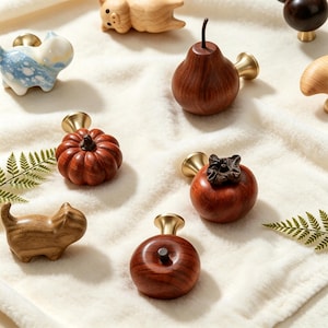 May include: A collection of decorative cabinet knobs featuring various shapes including a wooden pear, a pumpkin, a persimmon, a round fruit, a wooden cat, a light blue ceramic cat, a wooden pig, and a dark wooden sphere, all with brass bases.