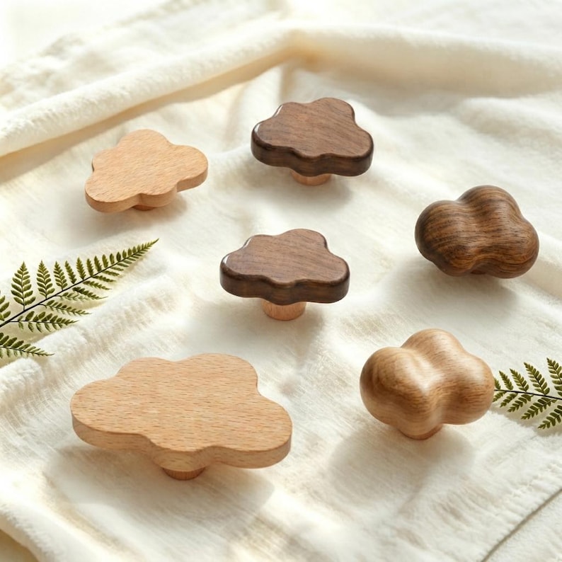 May include: A collection of six wooden cabinet knobs shaped like clouds, featuring varying shades of light and dark wood grain. The knobs have smooth, rounded edges and a polished finish, showcasing the natural texture and patterns of the wood.