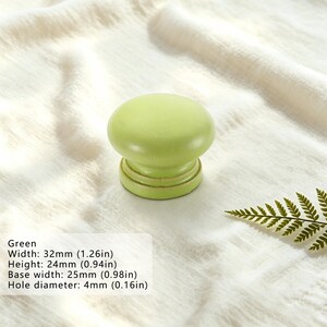 Puede incluir: Un pomo de mueble redondo de color verde claro con un acabado liso. El pomo tiene una anchura de 32 mm, una altura de 24 mm, una anchura de base de 25 mm y un di&aacute;metro de orificio de 4 mm, seg&uacute;n se indica en el texto del producto.