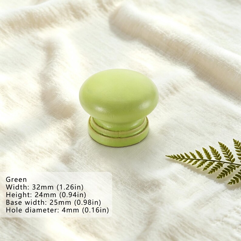 Puede incluir: Un pomo de mueble redondo de color verde claro con un acabado liso. El pomo tiene una anchura de 32 mm, una altura de 24 mm, una anchura de base de 25 mm y un di&aacute;metro de orificio de 4 mm, seg&uacute;n se indica en el texto del producto.
