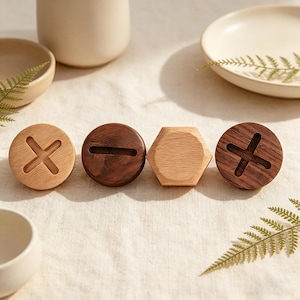 May include: Four wooden bottle stoppers in a row. Two are round with cross designs, one is a dark brown color and the other is light brown. The other two are a dark brown round stopper with a slot and a light brown hexagon-shaped stopper.