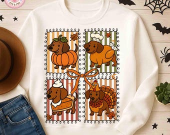 May include: White sweatshirt featuring a colorful graphic of dachshund dogs dressed in Thanksgiving-themed costumes. The dogs are depicted as a pumpkin, chef, slice of pie, and turkey. The design is framed with a decorative border and a large orange bow.