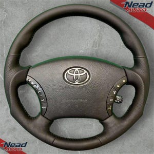 Pode incluir: Um volante preto da Toyota com um emblema prateado no centro. O volante tem controlos integrados e uma pega em couro perfurado. O airbag está rotulado. O fundo é cinzento neutro.