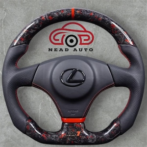 Puede incluir: Un volante de coche personalizado con un diseño de fibra de carbono negro y rojo. El volante presenta un agarre de cuero perforado negro con costuras rojas. El centro tiene un logotipo de Lexus y el texto "NEAD AUTO" es visible.