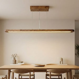 May include: A rectangular wooden pendant light fixture with a warm, glowing light. The fixture is suspended from the ceiling by thin wires and hangs above a wooden dining table. The light is a warm, inviting color.