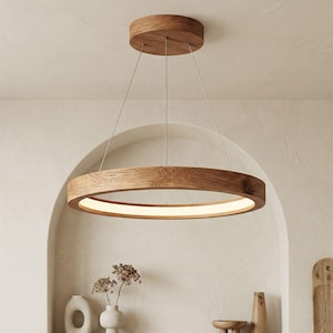 Puede incluir: Una moderna lámpara colgante circular de madera. La lámpara tiene un acabado de madera natural y una fuente de luz LED integrada. La lámpara se suspende del techo mediante finos cables, creando un diseño minimalista y elegante. El diámetro es de aproximadamente 60 cm.