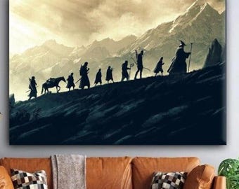 Op de afbeelding: Een canvas print met silhouetten van figuren die een heuvel beklimmen tegen een achtergrond van bergen. Het kunstwerk heeft een warme, sepia-getinte lucht en een donkere voorgrond. De figuren omvatten een paard en een tovenaar.
