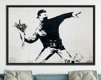 May include: Black and white framed artwork depicting a figure in a cap and face covering, throwing a bouquet of flowers. The figure is silhouetted against a white background, with the flowers in vibrant colors. The artwork is a modern, urban style.