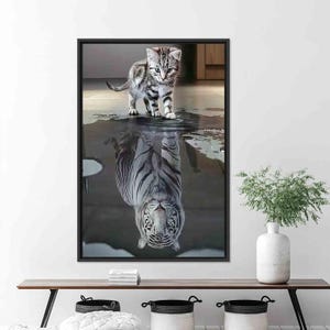 Puede incluir: Una impresión enmarcada que presenta un gatito de pie sobre su reflejo, que aparece como un tigre blanco. El gatito tiene rayas grises y negras. El reflejo del tigre tiene rayas negras. La imagen está en una habitación con suelo de madera.