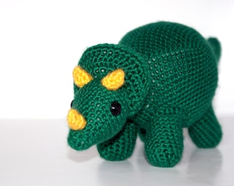 May include: A green crocheted triceratops dinosaur toy with yellow eyes and a black nose.