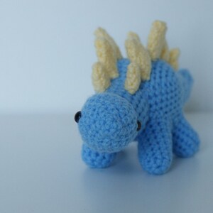May include: A blue crocheted dinosaur toy with yellow crocheted spikes on its back.