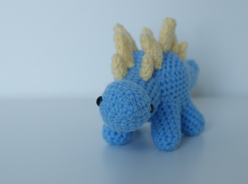 May include: A blue crocheted dinosaur toy with yellow crocheted spikes on its back.