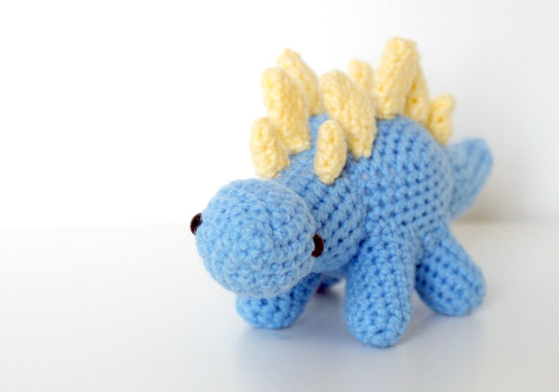 May include: A blue crocheted dinosaur toy with yellow spikes on its back.
