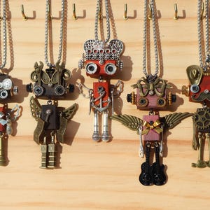 May include: A collection of steampunk robot pendant necklaces. Each robot has a unique design with gears, wings, and other mechanical elements. The robots are made of metal and wood, and hang from silver chains.
