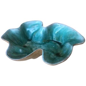 May include: A teal ceramic bowl with an unusual, organic form. The bowl has a glossy finish and a light brown rim. The interior features variations of teal and green hues, creating a marbled effect. This decorative bowl is suitable for serving or display.