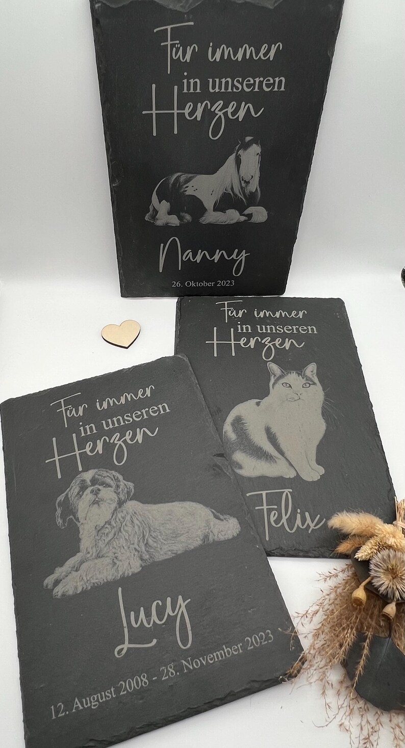 Puede incluir: Tres placas conmemorativas rectangulares de pizarra negra con im&aacute;genes grabadas de un caballo, un gato y un perro. Cada placa incluye el texto en alem&aacute;n "F&uuml;r immer in unseren Herzen", un nombre de mascota y fechas sobre fondo blanco.