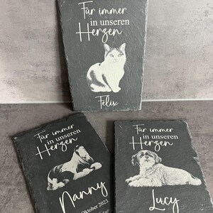 Puede incluir: Tres placas rectangulares de pizarra gris oscuro con grabados blancos de retratos de animales. Cada placa muestra la frase "F&uuml;r immer in unseren Herzen" sobre una ilustraci&oacute;n de un gato o perro y un nombre, incluyendo fechas en algunos.