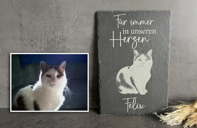 Puede incluir: Una placa rectangular de pizarra gris oscuro con una ilustraci&oacute;n blanca grabada de un gato sentado. Sobre el gato, el texto dice "F&uuml;r immer in unseren Herzen" y debajo del gato, el nombre "Felix" est&aacute; grabado en letras blancas.