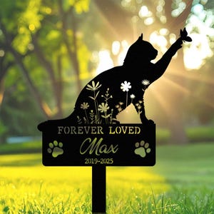 May include: Black metal cat silhouette garden stake with a butterfly, flowers, and the text "FOREVER LOVED Max 2019-2025". The cat is reaching for a butterfly. Paw prints are on the sign.