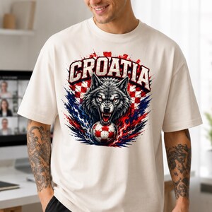 May include: An off-white short-sleeve t-shirt featuring a graphic print of a snarling wolf with red eyes positioned above a soccer ball. The design includes the word CROATIA in bold letters set against a red and white checkered background.