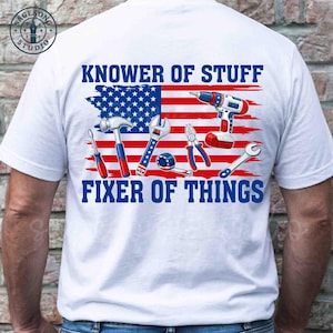 Puede incluir: Camiseta blanca con un gráfico que presenta herramientas y la bandera estadounidense. El texto dice "KNOWER OF STUFF FIXER OF THINGS" en azul. Las herramientas incluyen un destornillador, un martillo, una llave, unos alicates, una cinta métrica, un taladro y otra llave.