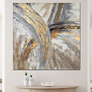 May include: Abstract wall art featuring gold, gray, and white brushstrokes. The artwork has a textured appearance with metallic gold accents. The painting is displayed above a wooden console table, adding a touch of elegance to the room.