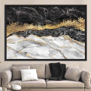 May include: Abstract framed art print featuring a marble design in black, white, and gold. The artwork has a black frame and is displayed above a beige sofa with pillows and a black throw blanket.