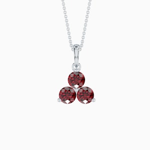 May include: A silver pendant necklace featuring three round, deep red gemstones arranged in a triangular cluster. The gemstones are set in a silver setting and suspended from a delicate silver chain.