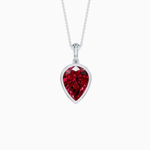 May include: A silver pendant necklace featuring a pear-shaped, faceted, deep red gemstone. The gemstone is set in a silver bezel and hangs from a delicate silver chain. The pendant is a classic and elegant piece of jewelry.