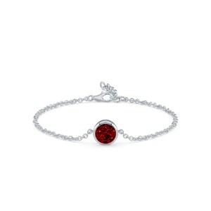 May include: A silver bracelet featuring a round, bezel-set, deep red gemstone. The delicate chain is connected to a lobster clasp. The gemstone is the focal point of this elegant piece of jewelry.