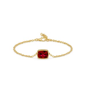 K&ouml;nnte beinhalten: Ein goldenes Armband mit einem leuchtend roten Edelstein. Der Edelstein ist rechteckig mit abgerundeten Ecken und in einer goldenen Fassung gefasst. Das Armband hat eine feine Kette und einen Verschluss.