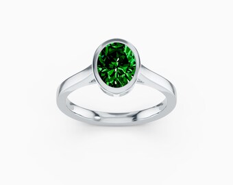 May include: A silver ring with a large, oval-cut, vibrant green gemstone. The gemstone is set in a bezel setting, and the band is smooth and polished. The ring is displayed against a white background, highlighting its elegant design.