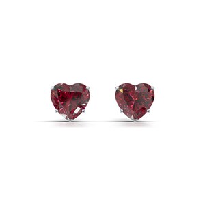 Puede incluir: Un par de pendientes de rubí en forma de corazón. Cada pendiente presenta una vibrante gema roja facetada engastada en un engaste de plata o metal blanco. Los pendientes se muestran sobre un fondo blanco, resaltando su color y forma.