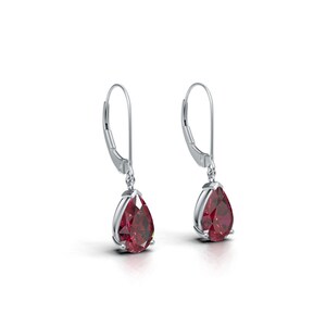 Puede incluir: Un par de pendientes colgantes de plata con piedras preciosas rojas en forma de pera. Los pendientes tienen un cierre de palanca y están engastados en un bisel de plata. Las piedras son facetadas.