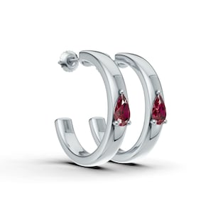 Peut inclure: Boucles d'oreilles créoles argentées avec une finition polie. Chaque boucle d'oreille est ornée d'une pierre précieuse rouge foncé en forme de poire. Fermeture à tige et poussette. Les pierres mesurent environ 0,6 cm de long.