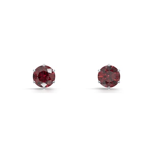 Può includere: Due orecchini a lobo con pietre preziose rosse rotonde. Ogni orecchino presenta una vibrante pietra rossa sfaccettata incastonata in una montatura in metallo argentato o bianco. Sono presentati su uno sfondo bianco.