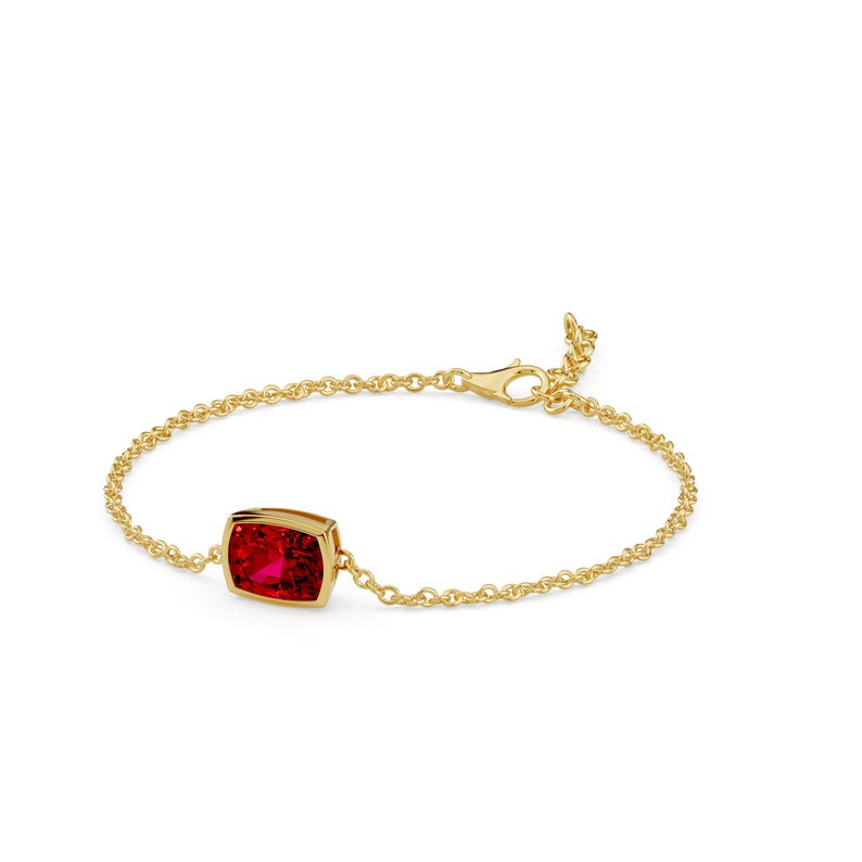 K&ouml;nnte beinhalten: Ein goldenes Armband mit einem leuchtend roten Edelstein. Der rechteckige Edelstein ist in einer goldenen L&uuml;nette gefasst und mit einer feinen Goldkette verbunden. Das Armband hat einen Karabinerverschluss.