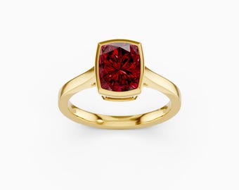 May include: A gold ring with a large, square-cut, deep red gemstone. The gemstone is set in a bezel setting, and the band is a simple, polished gold. The ring is shown against a white background.
