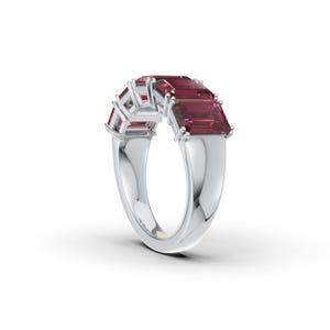Puede incluir: Un anillo de plata con una hilera de cinco piedras preciosas rectangulares de color rojo intenso en engaste de garras. La banda es lisa y pulida, con una estructura de metal sólido que se estrecha ligeramente hacia la base del anillo.