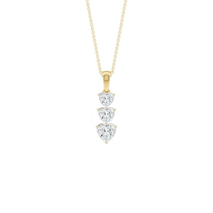 May include: A gold-colored necklace with three heart-shaped, clear gemstones. The gemstones are vertically aligned and suspended from a delicate chain. The pendant and chain are set against a white background, highlighting the jewelry's design.