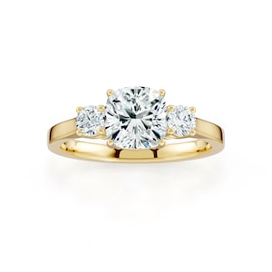 May include: A gold ring featuring a large, round, clear center stone flanked by two smaller, round stones. The ring's band is a polished gold color, and the stones sparkle against a white background. This three-stone ring is a classic jewelry piece.
