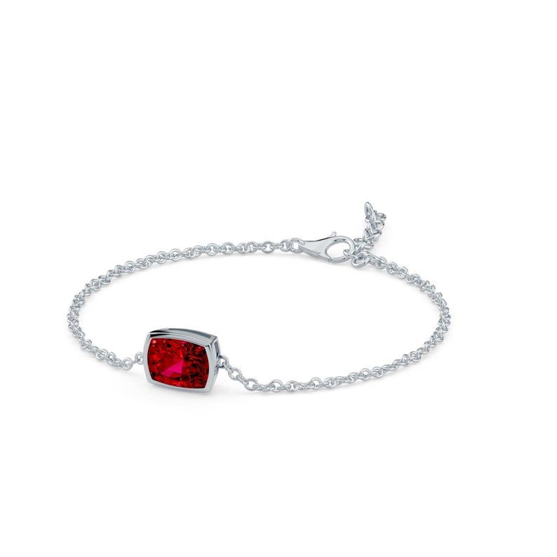 K&ouml;nnte beinhalten: Ein silbernes Armband mit einem rechteckigen, leuchtend roten Edelstein. Der Edelstein ist in eine Fassung gefasst und mit einer filigranen Kette verbunden. Das Armband hat einen Karabinerverschluss. Der Schmuck wird vor wei&szlig;em Hintergrund gezeigt.